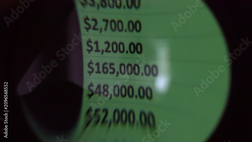 Close-up magnifying glass view of green financial numbers on a digital screen
