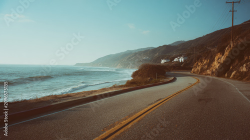 Coastal road along the sea, sun-faded summer colors, calm nostalgic atmosphere, analog film look, subtle grain texture, cinematic lighting, soft shadows, muted pastel tones, timeless summer memory