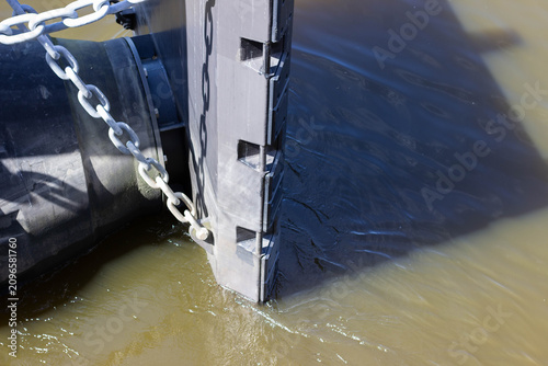 Fotografija Water barrier system with black plastic structure and chain submerged in murky w