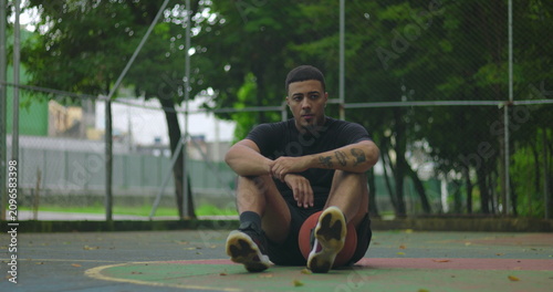 Obraz na plátně Preoccupied Latin Hispanic man sitting on outdoor basketball court holding ball