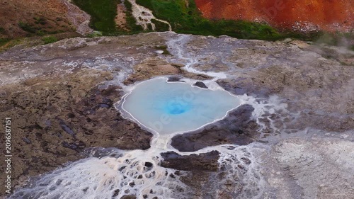 Aerial view of a steaming geothermal pool at Hverir Namaskard, Iceland. Gentle boiling and flowing outwash form white terraces over dark volcanic rock.