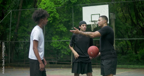 Tableau sur toile Three young men talking casually on outdoor basketball court, sharing jokes and