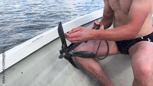 Close-up of a man unfolding a folding grapple anchor and dropping it into the lake water from a boat