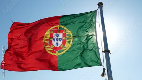 Flag of portugal waving against a clear blue sky with bright sunlight