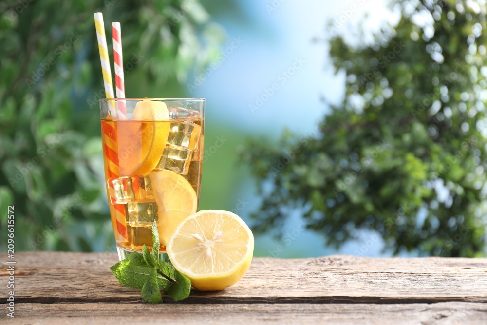 Fototapeta premium Refreshing ice tea with lemon and mint on wooden table outdoors, space for text