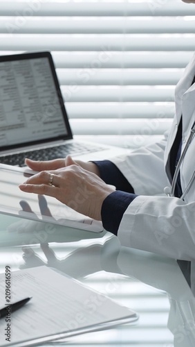 Healthcare professional wearing a lab coat and stethoscope, using a tablet and laptop, collaborating with technology for medical research, digital records, and remote patient care