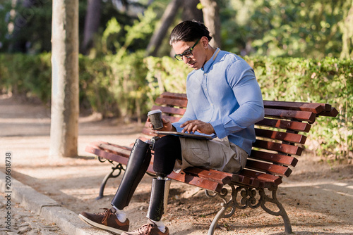 Latino man with disability using tablet on park bench