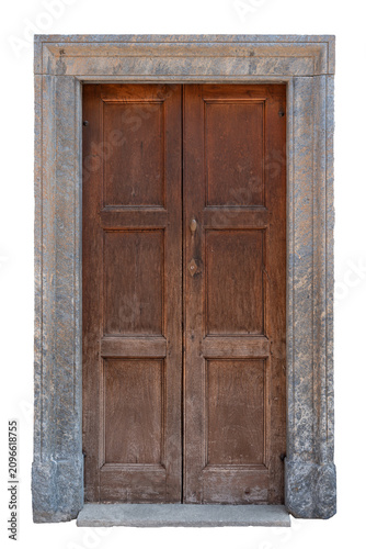  Old traditional European entrance featuring weathered brown wooden double doors with rectangular panels and a vintage metal handle, framed by a classic rustic grey stone portal and threshold