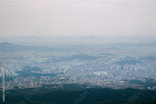 Panoramic Seoul skyline surrounded by mountains and forested hills under hazy atmosphere