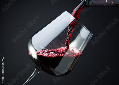 Slika na platnu Red wine is pouring into a glass from a bottle, close up