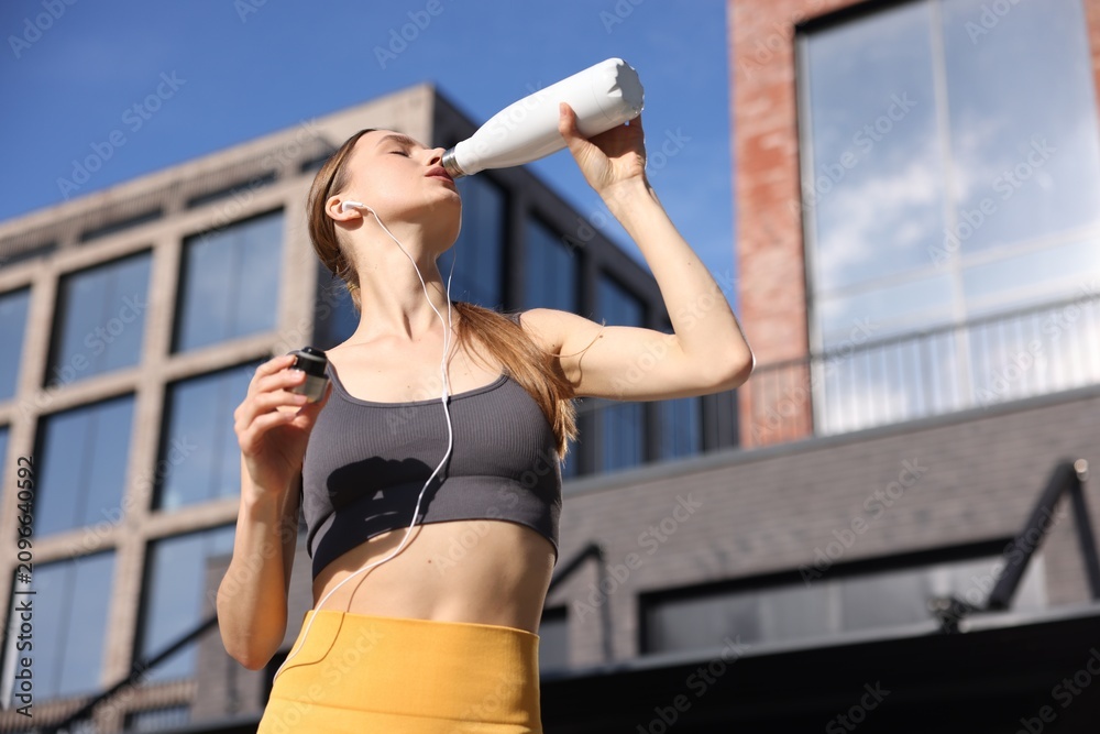 Obraz premium Woman in sportswear drinking water outdoors on sunny day, low angle view. Space for text