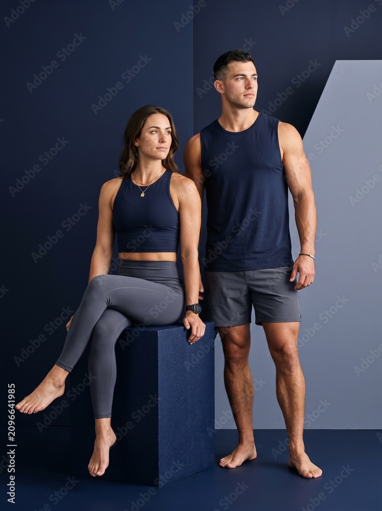 Fototapeta premium Athletic Caucasian Couple in Matching Navy Charcoal Beachwear Posing on Studio Block, Premium Resort Wear Fitness Editorial Portrait