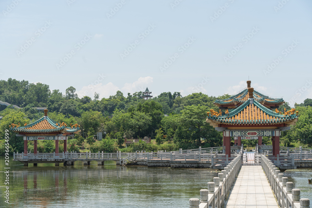 Fototapeta premium Scenic view of a traditional Chinese pavilion and bridge corridor across a peaceful lake under blue sky