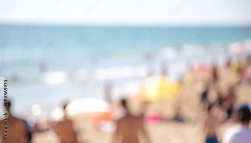 Obraz premium Blurred beach background featuring unrecognizable people relaxing on sandy shore during a sunny summer day with soft natural lighting