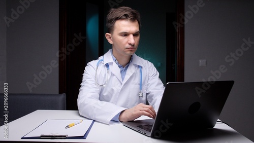 Fotografie Male doctor wearing a white lab coat and stethoscope, intently typing on a lapto