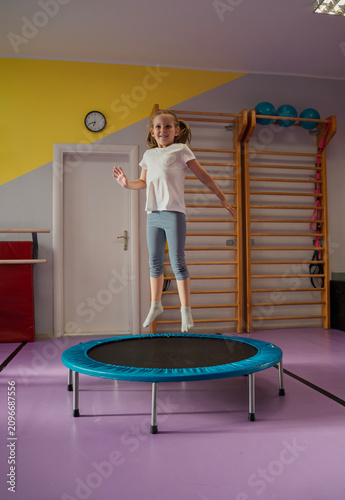 One cute little girl jumping on trampoline alone in the gym indoors