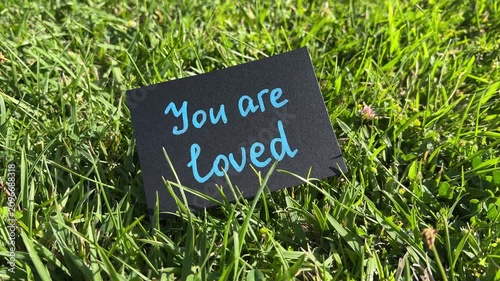 You are loved - black note with encouragement and support text on the grass in the background