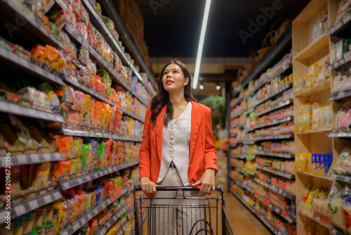 Tableau sur toile Woman pushing shopping cart choosing products in supermarket aisle