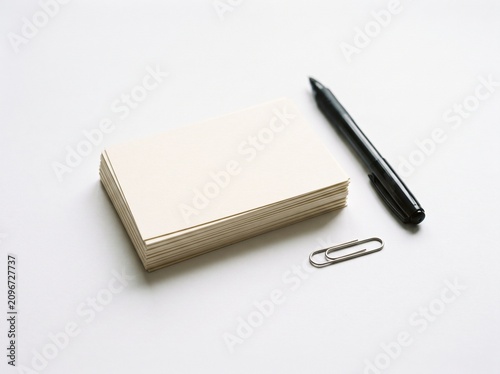 Stack of blank cream colored index cards with a black pen and paperclip on a clean white background for study and organization