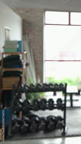 Vertical video: Raising arm, woman in pink top with watch warming up revealing dumbbell rack in gym