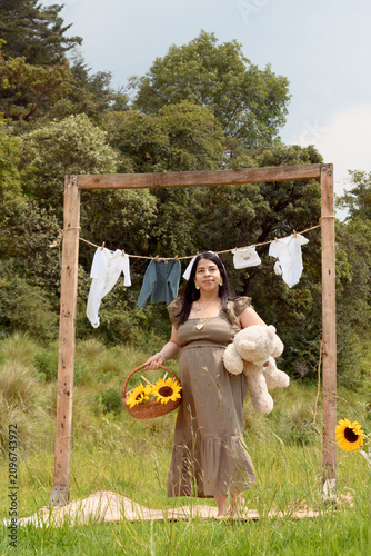 Full Shot of Pregnant Hispanic Woman Standing with Teddy Bear and Sunflower Basket