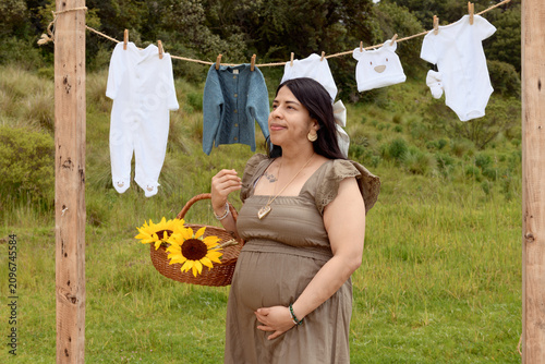Medium Shot of Pregnant Hispanic Woman with Sunflower Basket and Baby Clothesline