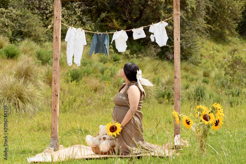 Profile View of Pregnant Woman Kneeling Holding Sunflower in Meadow
