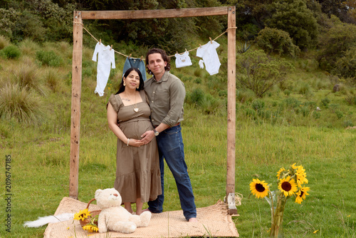 Full Shot of Pregnant Hispanic Couple Embracing in Meadow Setup
