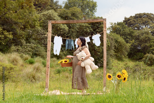 Full Shot of Pregnant Hispanic Woman Standing with Teddy Bear and Sunflower Basket