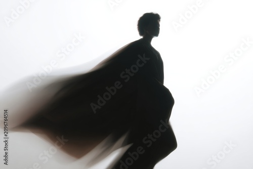 Dramatic silhouette of a figure with flowing cloak for minimalist poster and editorial background in dynamic motion pose