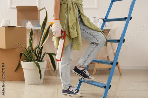 Bild auf Leinwand Young woman with sealant climbing stepladder in room