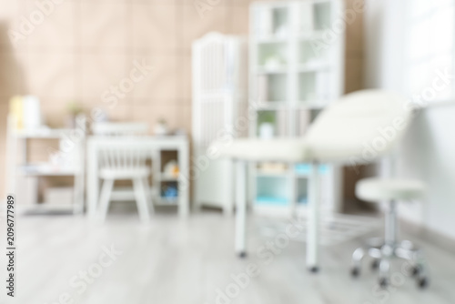 Blurred view of medical office with couch, doctors workplace and shelf units