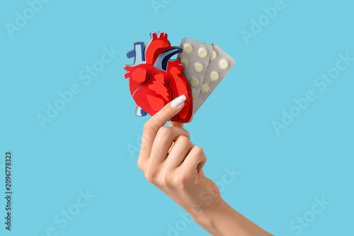 Young woman with paper heart and pills on blue background, closeup
