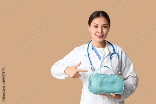 Asian female doctor pointing at first aid kit on brown background