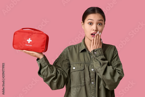 Shocked young Asian woman with first aid kit on pink background