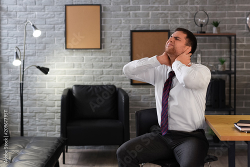 Businessman suffering from neck pain in office at night