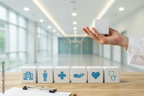 Hand holding a white cube with medical icons on a wooden table in a hospital clinic setting