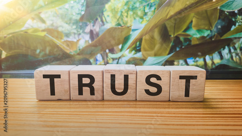 Tableau sur toile Trust wooden blocks spelling word TRUST with green foliage background symbolizin