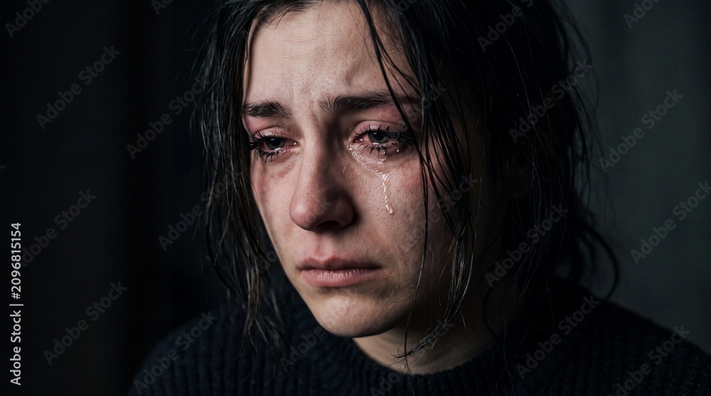 Fototapeta premium Emotional Portrait of a Depressed Young Woman Crying with Tears and Red Eyes on Dark Background