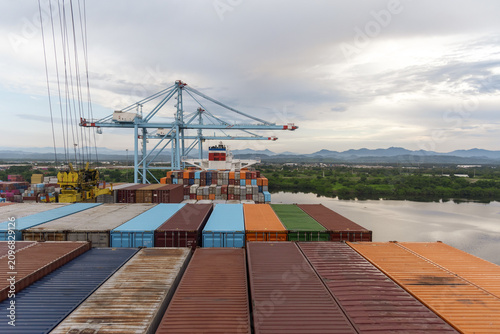 Maritime transport and global trade scene at Lázaro Cárdenas port, Mexico. Container ship loading operations with gantry cranes and colorful cargo containers against a mountainous background.