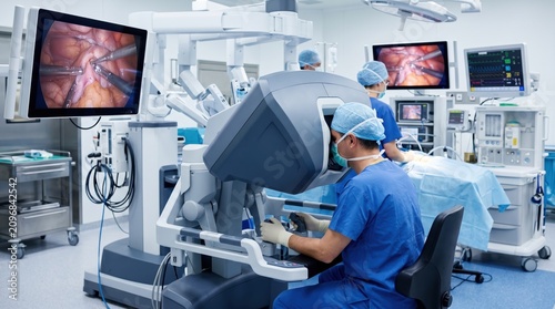 Medical surgeon operating advanced robotic surgical system in modern hospital operating room, minimally invasive procedure with high definition monitors displaying internal anat...