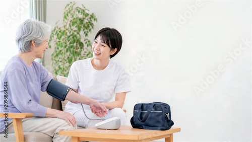 自宅で高齢女性の血圧を測定する訪問看護師と訪問看護バッグ