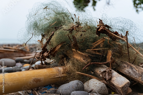 Weathered fishing net stranded on a rocky beach, tangled with driftwood and stones, highlighting marine pollution and coastal conservation