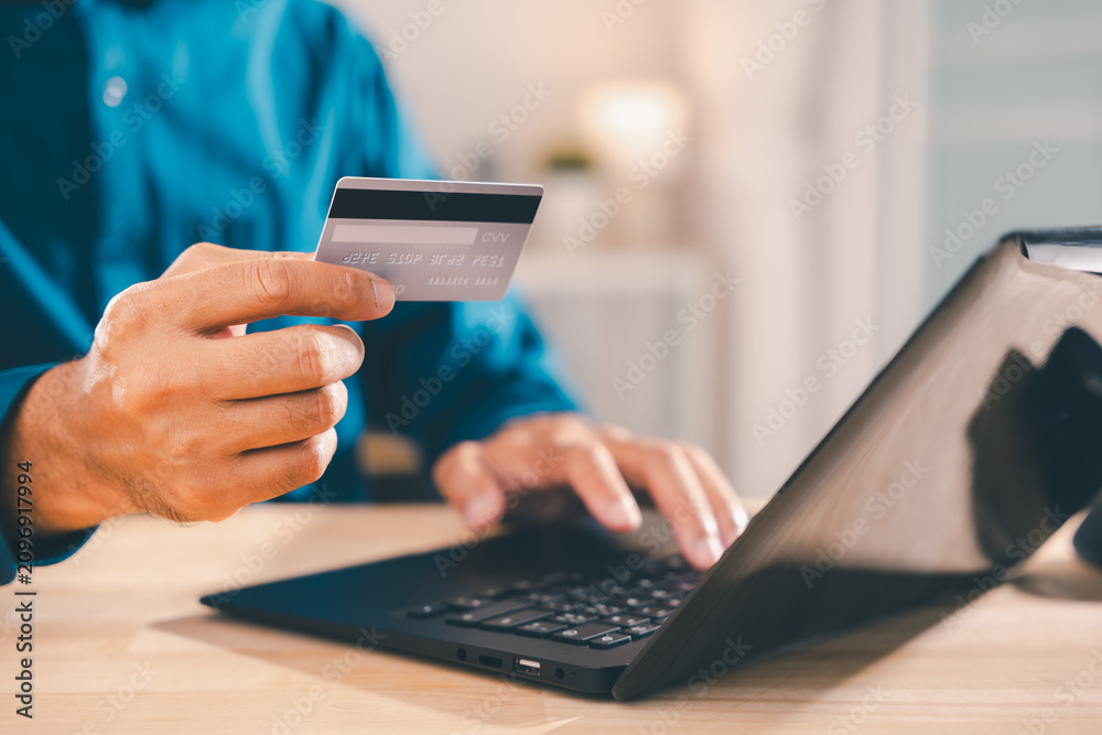 Fototapeta premium Person holding smartphone for shopping online and payment banking while typing on laptop computer keyboard with plastic credit card for secure transaction at wooden desk