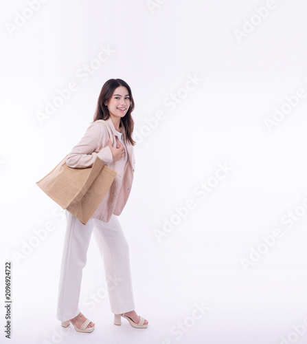 Foto Smiling young Asian businesswoman in a beige suit carrying a large eco-friendly jute shopping bag on an isolated white background