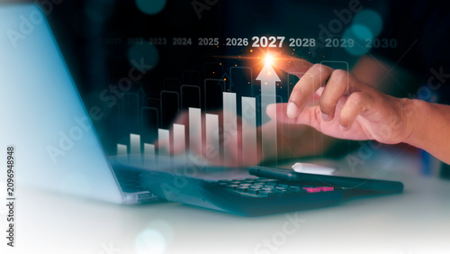 Businessman pointing at rising arrow on financial growth chart targeting the year 2027 success.