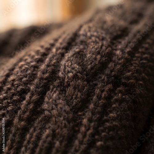 Close-up of dark brown knitted wool fabric texture. Soft cozy winter material for fashion design and home decor projects.
