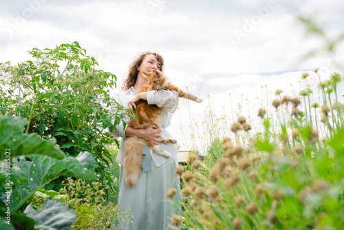 Woman cuddling a young Maine Coon cat in a sunny vegetable garden  