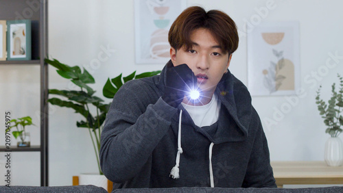 Konstfotografi Young Asian Man in Hoodie Holding Flashlight in Living Room