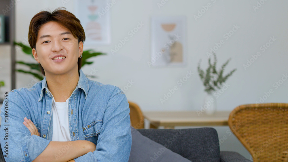 Obraz premium Smiling Young Asian Man with Arms Crossed in Bright Living Room
